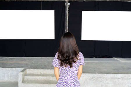 A woman standing and looking at a blank picture frame on a white wall art galleryの写真素材
