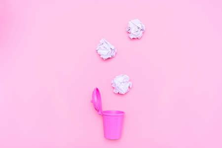 Wrinkled paper is about to fall into pink trash on a pink background.の写真素材