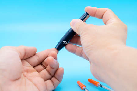 Diabetes test. Man hands checking blood sugar level by Glucose meter on blue background, copy space