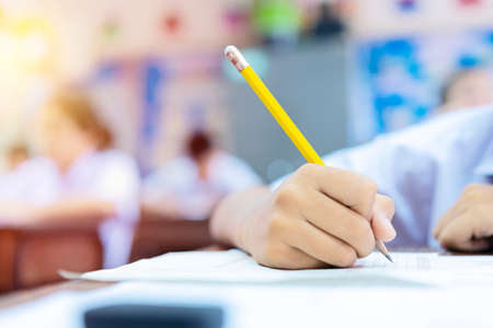 School students hard at work in the classroom sitting with his head on his hand reading and writing notes on sheets of white paper, taking exam conceptの写真素材