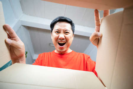 The surprised man unpacking, opening carton box and looking inside. The package, delivery, surprise, gift lifestyle concept. Human emotions and facial expressions conceptsの写真素材