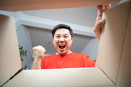 Man sitting on couch in living room and opening carton box. Cheerful girl getting parcel at home. Mail delivery to house.の写真素材