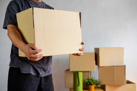 Midsection of man carrying open cardboard box in new home, cropped shot of man holding cardboard boxes while moving homeの写真素材