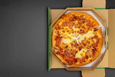 Pizza in a cardboard box on a black chalkboard background. Space for text. View from above. Pizza delivery. Pizza menu.の写真素材