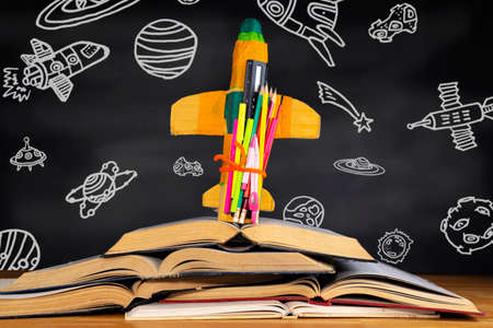 Education concept and back to school A cardboard rocket placed over a book in front of a blackboard depicting space objects in the classroom.の写真素材