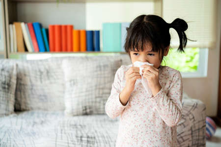 Runny nose. Sick little girl blowing her nose and covering it with handkerchiefの写真素材