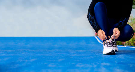 Runner woman tying up laces of shoes, getting ready to run for cardio and weight loss, no face. Sportive wear in trend colors - vibrant coral neon color, long crop bannerの写真素材