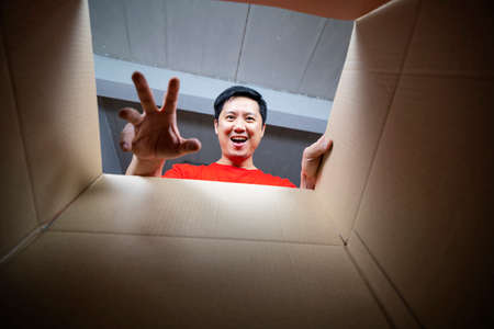 The surprised man unpacking, opening carton box and looking inside. The package, delivery, surprise, gift lifestyle concept. Human emotions and facial expressions conceptsの写真素材