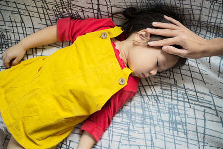 Closeup photo of caring mother holding head on sick daughter forehead, woman checks temperature to the childの写真素材