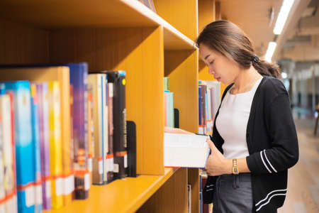 Asian woman reading a book in library. Portrait of college girl reading book in libraryの写真素材