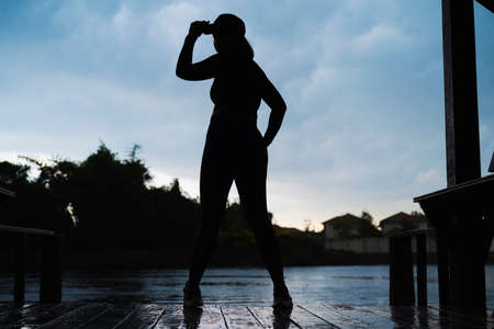 Young woman silhouette exercise, standing on the lake in the park. The atmosphere in the morning with heavy rainの写真素材