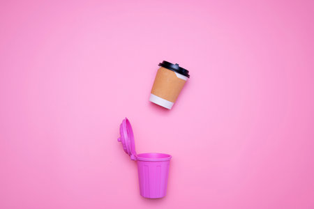 Paper coffee cups are about to fall into pink trash on a pink background.