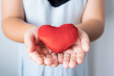 Heart in child hands. Girl giving love to someone. Red heart on cover. Girl made donation to heart. Valentine day of love concept and Healthcare concept.の写真素材