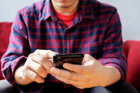 Glad fashionable young bearded guy wears stylish clothes and denim shirt, has trendy hairstyle, happy to exchange messages with friends, uses free internet connection on electronic modern gadgetの写真素材