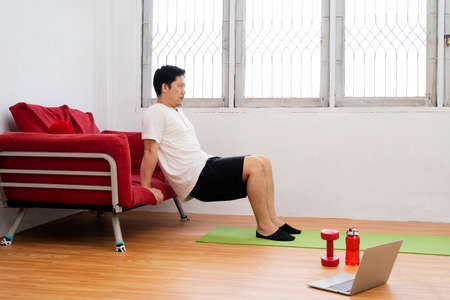 Fitness workout at home. Healthy fit man doing triceps dips exercise in the living room.の写真素材