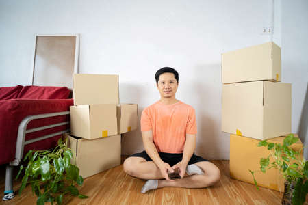 Happy man moving to a new house Sitting happily resting. Young man with cardboard boxes on wall backgroundの写真素材