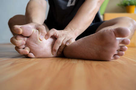 Man suffering from foot pain or numbness at home. Causes of pain include plantar fasciitis, gout, arthritis, tendinitis, diabetic neuropathy or overuse injuries. Healthcare concept. Close up.の写真素材