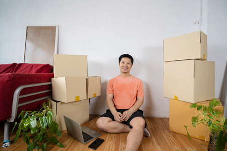 Man having break during moving to new house using laptop. Cardboard boxes - moving to a new houseの写真素材
