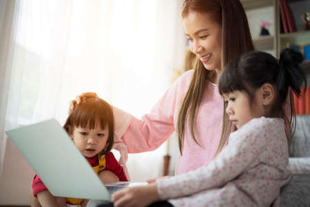 Loving mother resting relaxing with little preschool daughter together spend free time on weekend have fun using computer. Family surfing internet watch cartoons funny videos making video callの写真素材