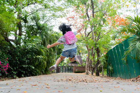Back to school. Cute asian child girl with backpack running, jumping and going to school with funの写真素材