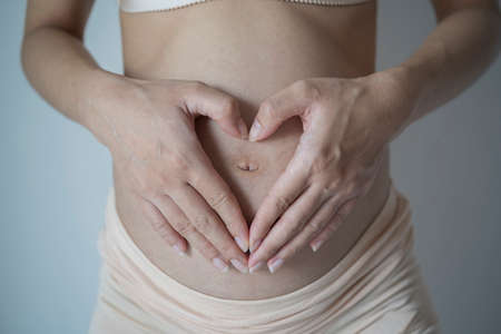 Beautiful young pregnant woman making heart with her hands, closeupの写真素材