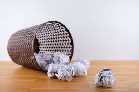 Crumpled paper balls all around a black recycle bin. Placed in the background behind a white wall
