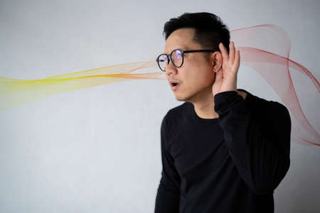 Man holding hand near ear trying to listen to interesting news expressing communication concept. Hearing test showing ear of man with sound waves simulation technologyの写真素材