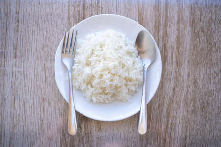 plate of white rice with spoon and fork was placed on the dining table,  Jasmine rice on white plate from Thailand Asiaの写真素材