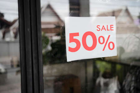 Sale signs in shop window, big reductions. Red sign hanging on a glass window with the inscription sale up to 50% offの写真素材