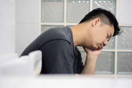 young sleepy man sits on toilet want to sleep, after returning from the hangout.の写真素材