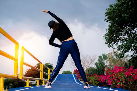 Young beautiful Asian woman in sports outfits doing stretching before workout outdoor in the park,...