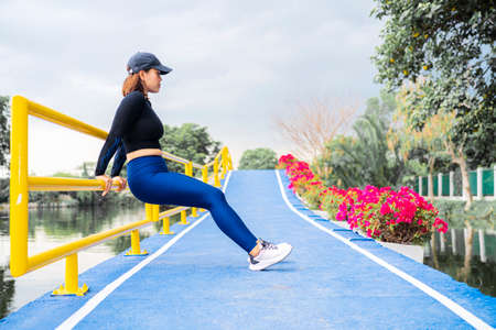 Young beautiful Asian woman in sports outfits doing stretching before workout outdoor in the park in...