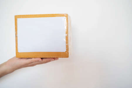 Hand holding a brown paper box with white label isolated on white background