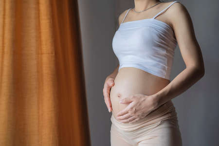 pregnancy, motherhood, people and expectation concept - close up of happy pregnant woman with big belly at windowの写真素材