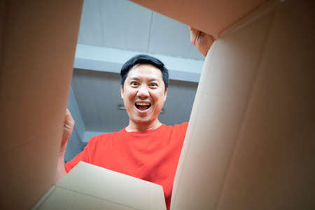 Smiling man opening a carton box and looking inside, relocation and unpacking conceptの写真素材