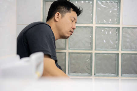young sleepy man sits on toilet want to sleep, after returning from the hangout.の写真素材