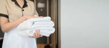 Change of towels in the hotel room. A uniformed maid is cleaning up the hotel room.Towels in the hands of the maid. An unrecognizable person. The concept of the hotel business. Photos in the interior.の写真素材