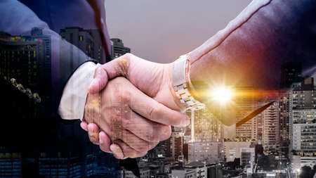 Double exposure of business handshake for successful of investment deal and city night background, teamwork and partnership concept.の写真素材