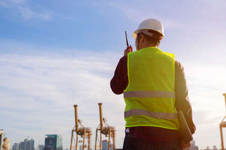 Engineers and crane.smiling dock worker holding radio and ship background, foreman, worker holding radio communication to controlの写真素材