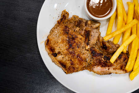 juicy grilled pork chop (neck cut) with greens. Grilled steaks, baked potatoes and vegetable saladの写真素材
