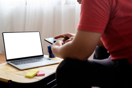 Happy millennial businessman relaxing with smartphone at workplace in home, leaning back in chair, texting with friends or browsing internet, having break in work, sitting at desk with laptopの写真素材