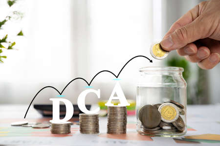 Saving Coins, Saving Money. Hand of Business man putting coins in glass bottle with stack coin and text DCA for business, share, marketing, finance and accounting concept.の写真素材