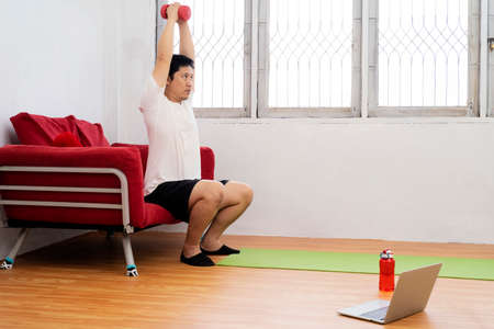 Strong athletic fit man in T-shirt and shorts is doing calf raise exercises with dumbbells at home. Sport, healthy lifestyle.の写真素材