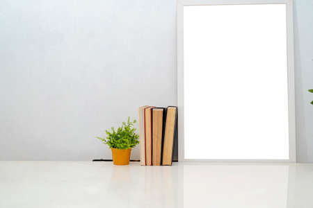 Breakfast still life. Cup of coffee, books and empty picture frame mockup on desk, table. Vase with olive branches. Elegant working space, home office concept. Scandinavian interior design.の写真素材