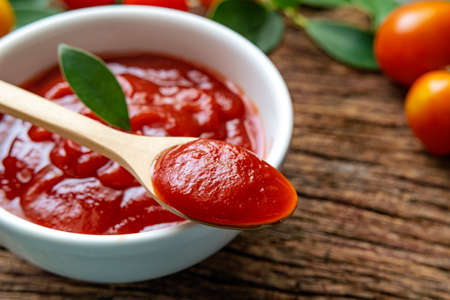 Close up of ketchup and tomatoes placed on a wooden background. Scoop ketchup with a spoon.の写真素材