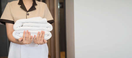 Cropped image of a maid in uniform holding stacks of clean towels in a hotel suite.の写真素材