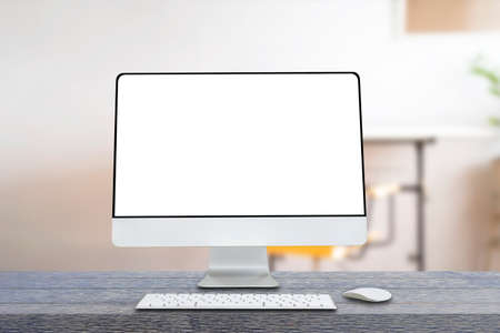Computer monitor with white blank screen putting on wooden working desk with wireless mouse and keyboard over blurred vintage office as background.の写真素材