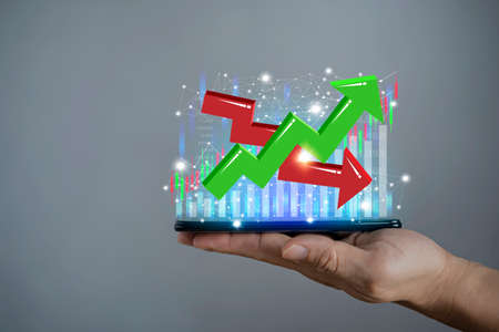 Businessman holding a phone, sales dynamics in the market. Close up of smart phone with creative forex chart on blue background. Trade, finance, technology and communication concept.の写真素材