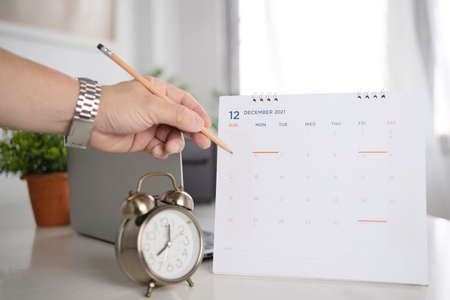 Hand with pen mark calendar. Hand holding a pencil writing on the calendar to prepare for the event in December of 2021.の写真素材