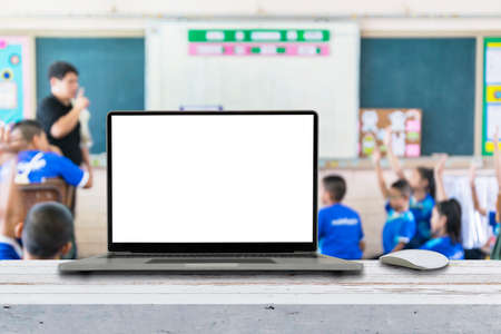 Computer on the table, blur image of children in the classroom as background.の写真素材